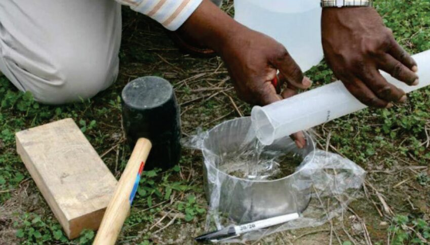 Close-up of a person pouring water into a metal ring set in the soil during an infiltration test.